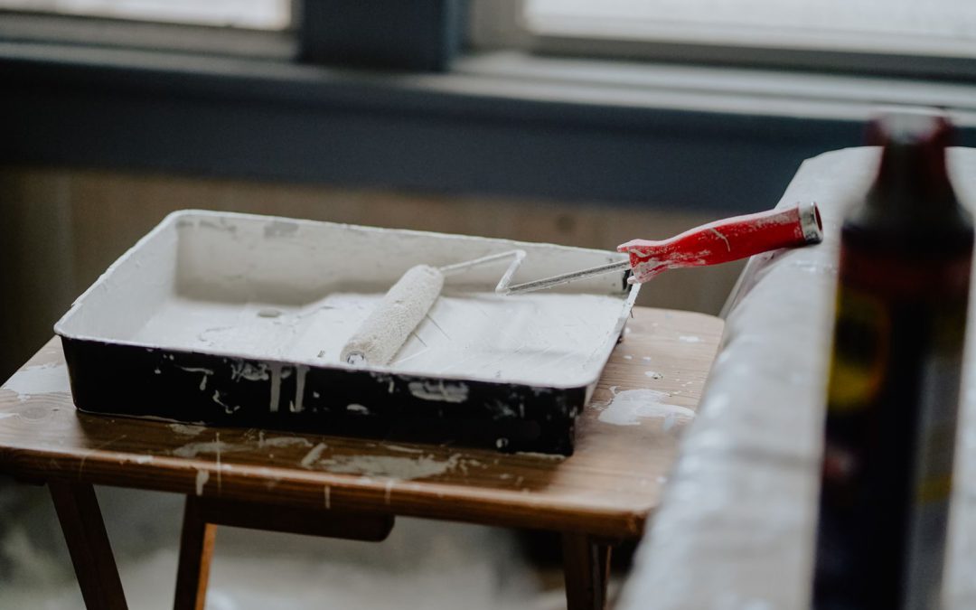 A paint roller and tray with white paint on a wooden table, indicating a renovation work.